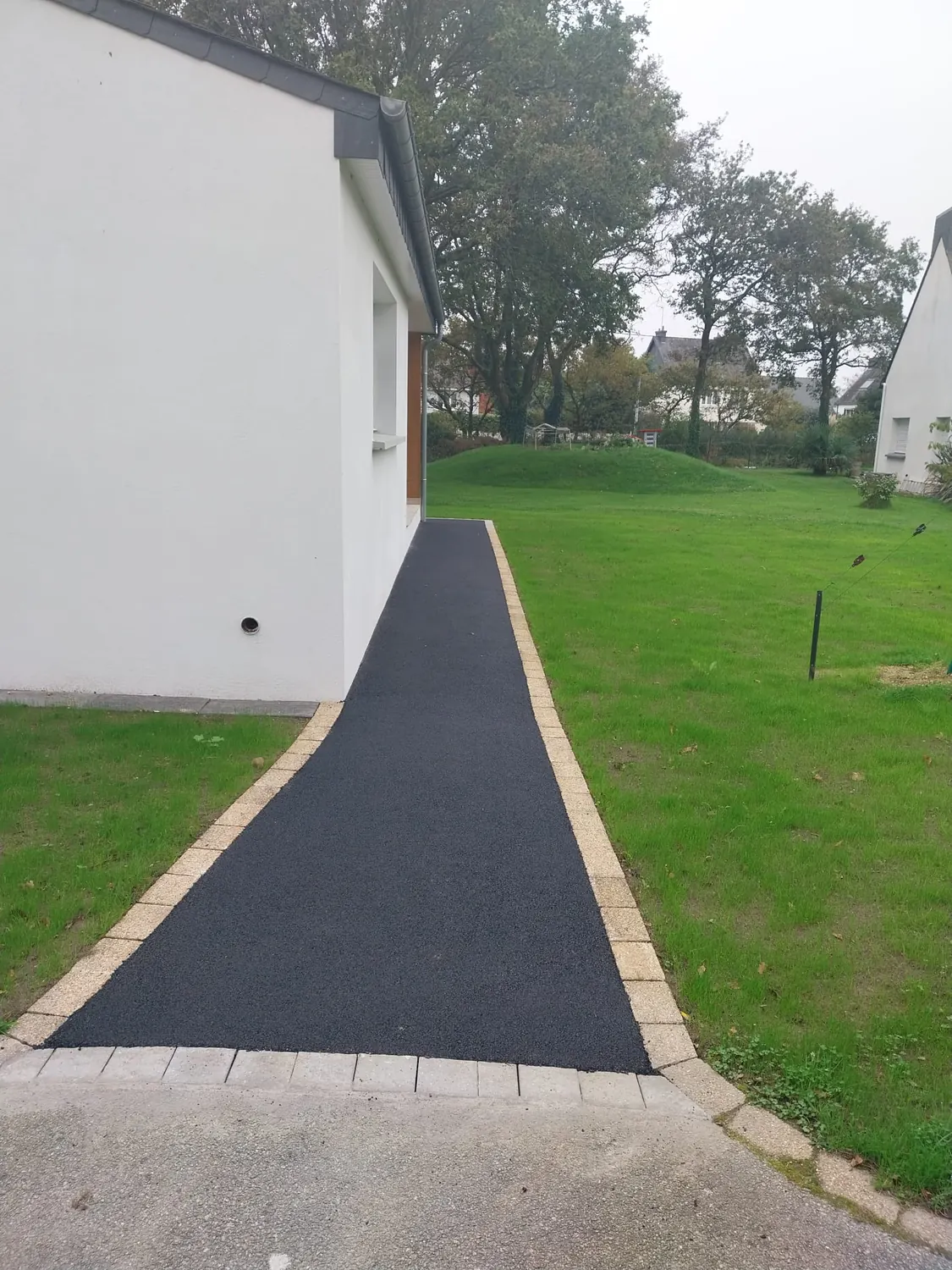 Allée piétonne en enrobé bordée de pavés le long d'une maison