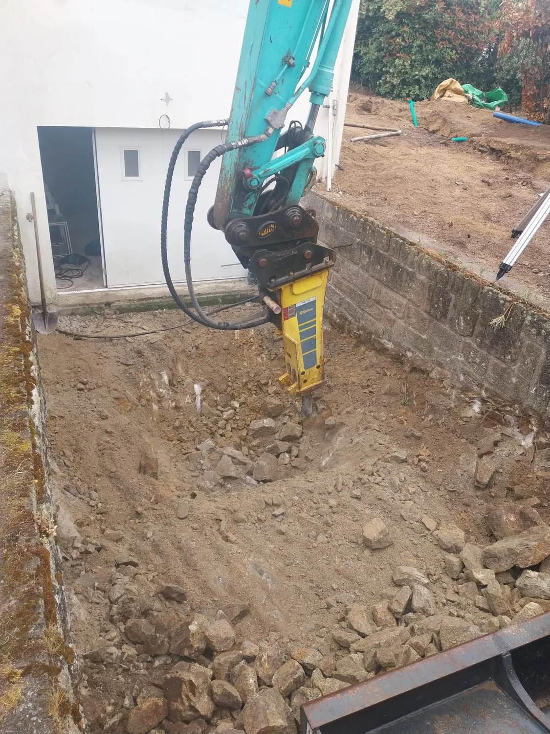 Brise-roche hydraulique au travail dans une fouille contre un mur
