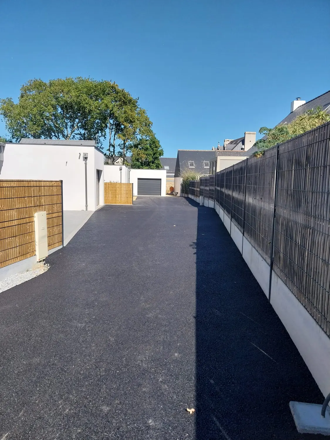 Allée en enrobé neuf longeant un muret et une clôture ajourée