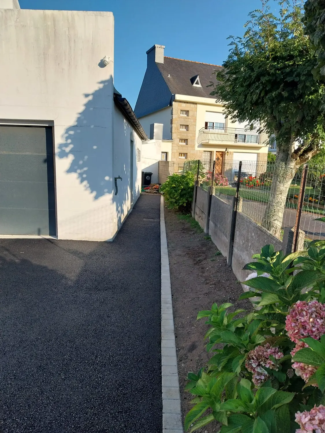 Allée étroite en enrobé entre un mur blanc et des hortensias