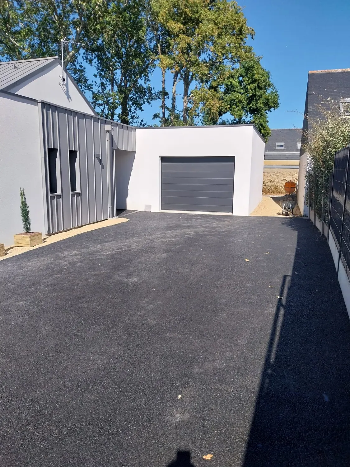 Enrobé noir menant à un garage, bordure gravillonnée et haie