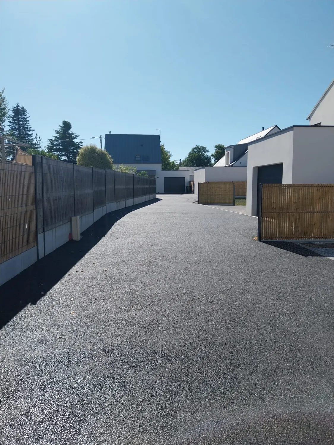 Longue allée en enrobé le long d'une clôture bois et béton
