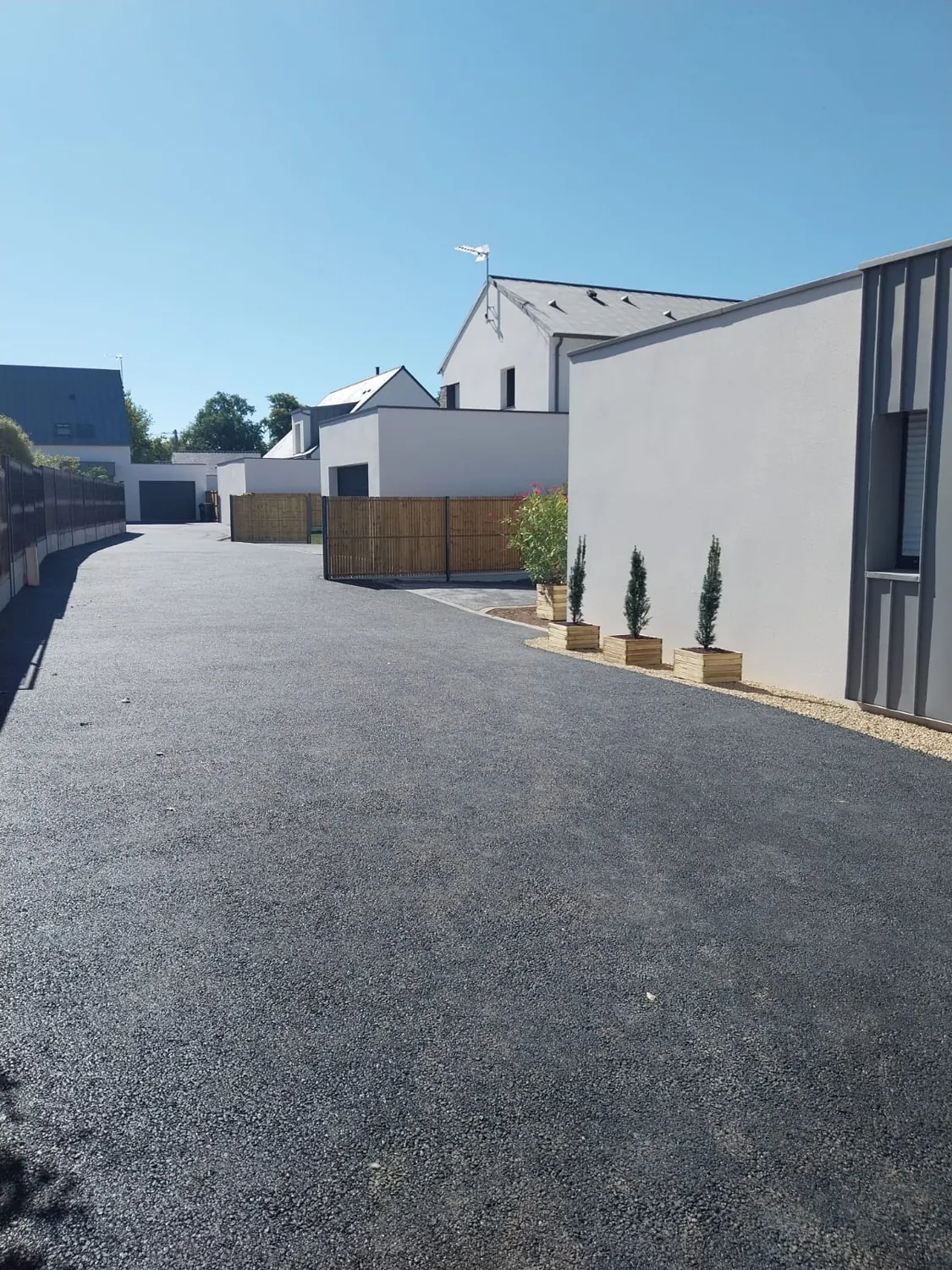 Allée en enrobé en perspective entre clôtures et maisons neuves