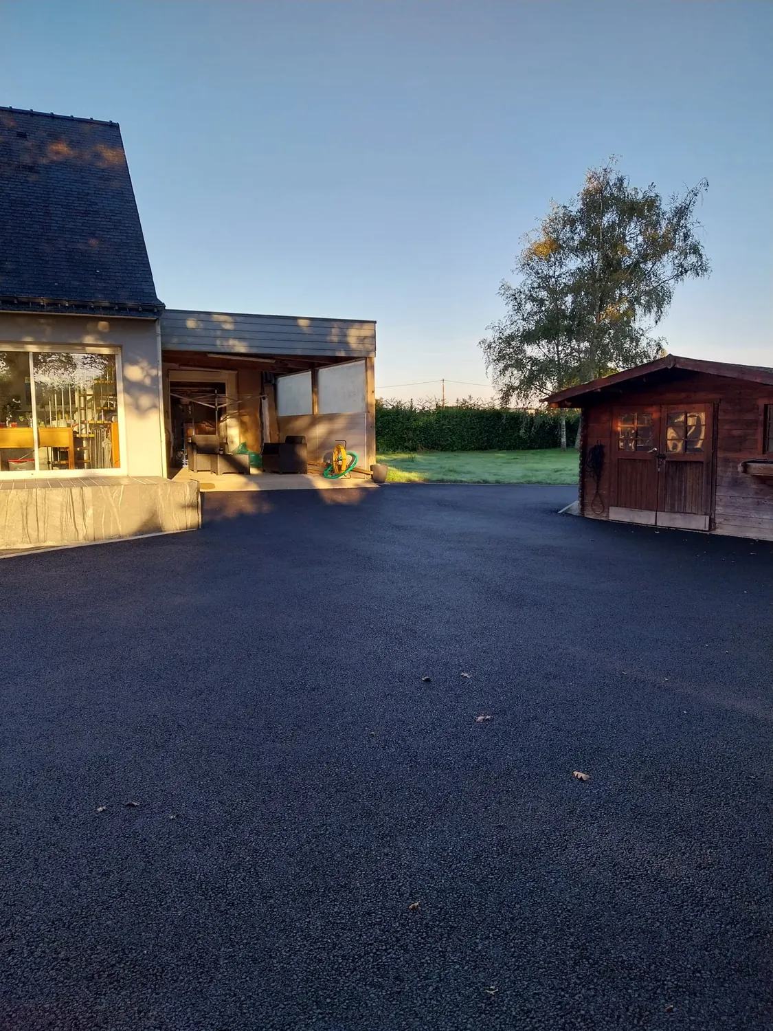 Cour en enrobé neuf devant un cabanon bois et une maison (après)