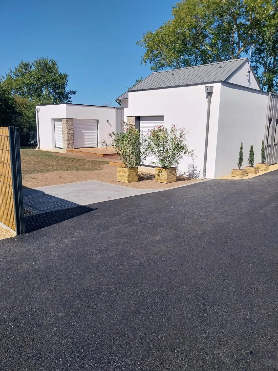 Cour en enrobé avec bordure béton et jardinières devant une maison