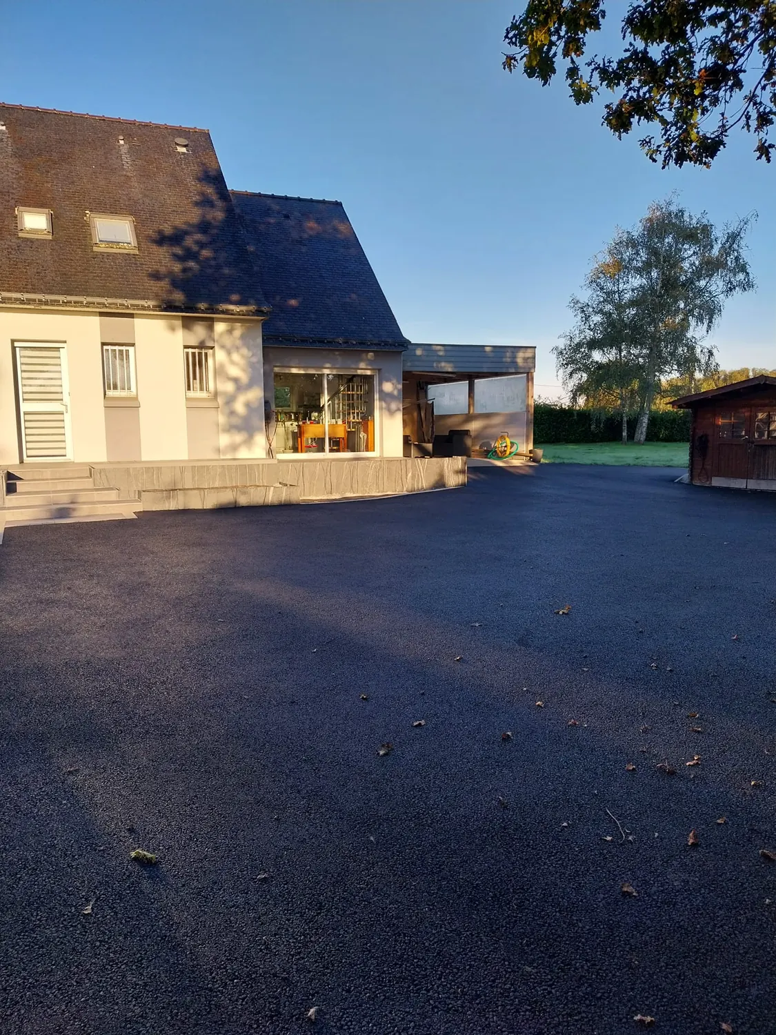 Grande cour en enrobé devant une maison à toiture ardoise