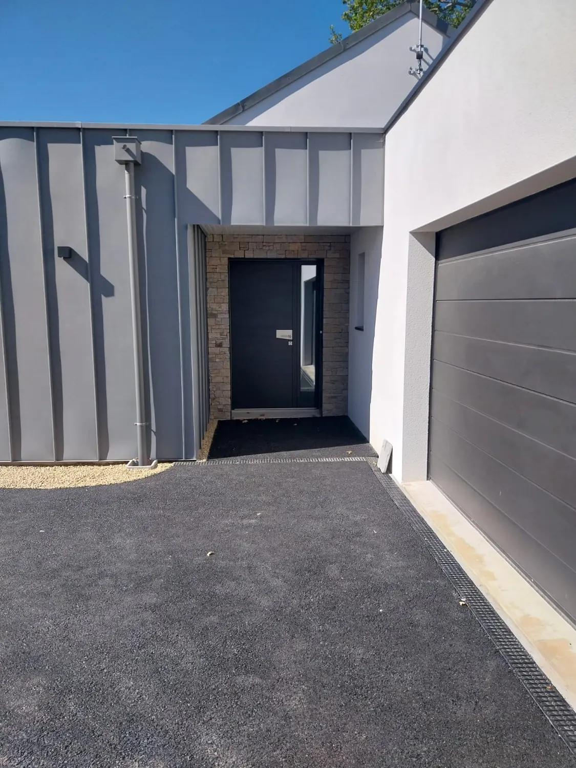 Entrée d'une maison contemporaine avec enrobé neuf et caniveau à grille