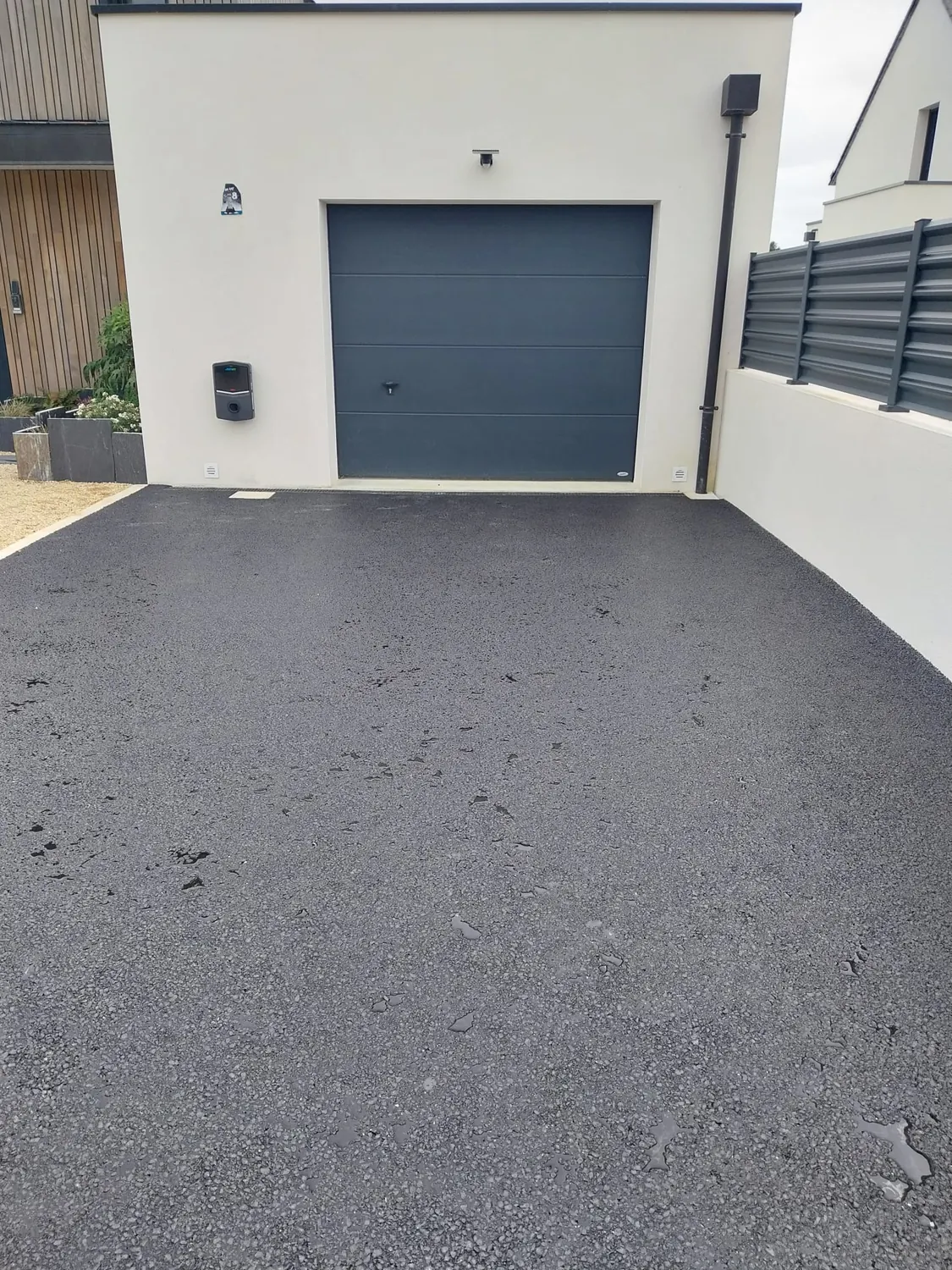 Enrobé neuf devant un garage gris avec muret blanc et clôture aluminium