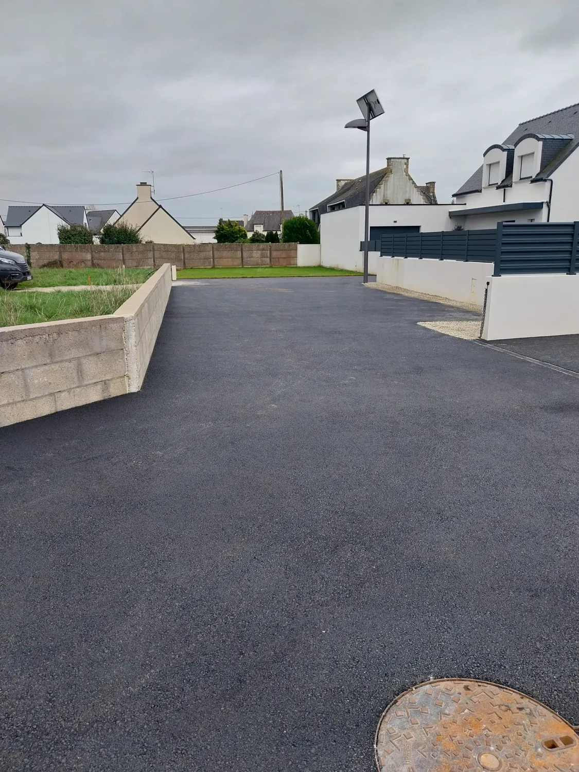 Enrobé neuf dans un lotissement, muret béton et pelouse
